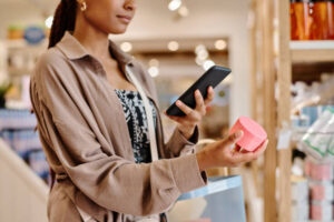 Close-up of young woman making photo of cream on her smartphone during shopping in the store